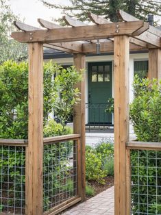 a wooden arbor in front of a house with green doors and plants on the side