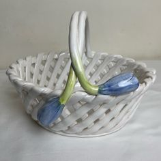 two blue flowers in a white basket on a tableclothed surface, with one flower bud sticking out of it