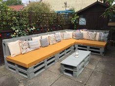 an outdoor couch made out of pallets with pillows on it and some plants in the background