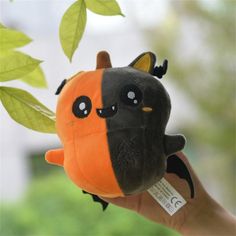 a hand holding an orange and black stuffed animal with green leaves in the back ground