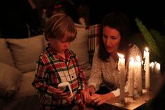 a woman and child lighting candles on a table in front of a couch with christmas decorations