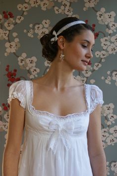 a woman in a white dress standing next to a wall with floral designs on it