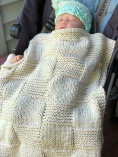 a baby wrapped up in a blanket and wearing a knitted hat is sitting in a stroller