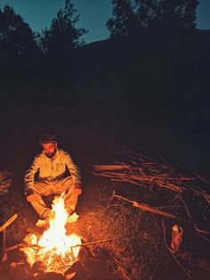 a man sitting in front of a campfire at night