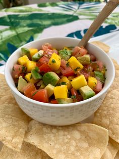 a white bowl filled with fruit and salsa next to tortilla chips on a table