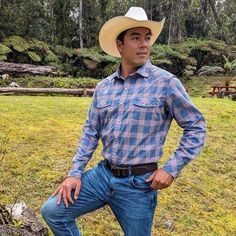 a man wearing a cowboy hat standing in the grass with his hands on his hips