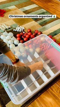 a child is playing with christmas ornaments in a plastic container on the floor next to other holiday decorations