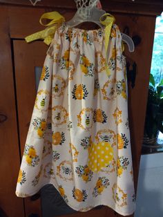 a yellow and white dress hanging on a clothes rack in front of a wooden cabinet