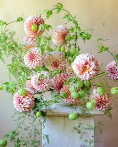 a vase filled with lots of pink flowers on top of a white table next to green leaves