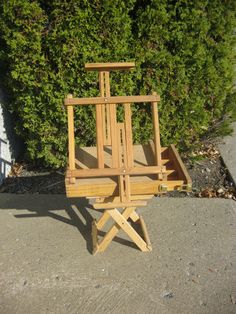 a wooden easel sitting on top of a cement ground next to a green bush