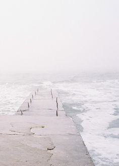 a person walking along the edge of a pier with an umbrella over their head, on a foggy day