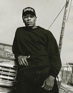 a black and white photo of a man leaning against a car