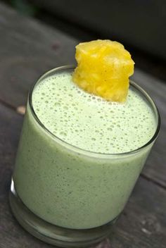 a green smoothie with a yellow piece of fruit on the top, and a straw sticking out of it