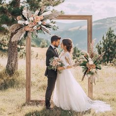 a bride and groom standing in front of a wooden frame with floral arrangements on it