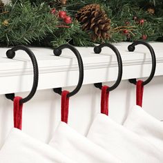 christmas stockings hanging from hooks on a mantle with pine cones and evergreen branches in the background