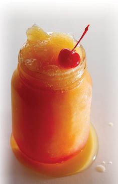 an orange drink with a cherry on the top sits in a small glass jar and garnished with sugar