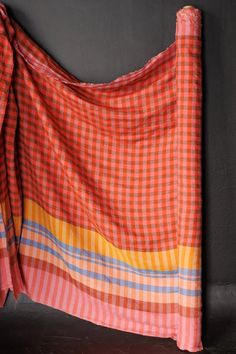 an orange and blue checkered blanket hanging on the wall next to a gray wall