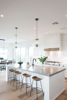 a kitchen island with four stools in front of it and lights hanging from the ceiling