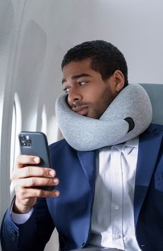 a man in a blue suit is using his cell phone while wearing a neck pillow