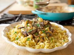 pasta with mushrooms and peas in a white bowl on a wooden table next to a skillet