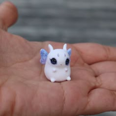 a tiny white toy with blue eyes sitting on someone's hand