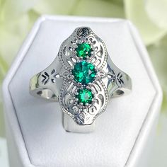 The central emerald, full round cut and 5mm in diameter, is flanked by two smaller 4mm gemstones, creating a symphony of glamour and sophistication. The quality of the setting is guaranteed with a marked 925 sterling silver inscription inside the band, ensuring lasting beauty and integrity. Vintage Emerald Open Ring For Anniversary, Vintage Open Emerald Ring For Anniversary, Vintage Green Crystal Open Ring, Victorian Silver Metal Rings, Vintage Green Crystal Ring For Anniversary, Elegant Metal Rings With Intricate Design, Victorian Style Silver Metal Rings, Vintage Open Ring Jewelry With Intricate Design, Vintage Open Ring With Intricate Design