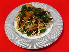 a white plate topped with noodles and vegetables on top of a red tablecloth covered table