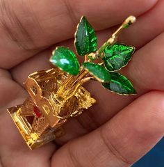 a gold brooch with green leaves on it in the palm of someone's hand