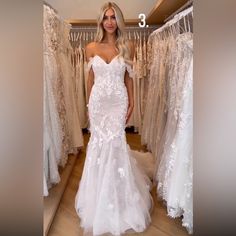 a woman in a wedding dress standing next to dresses hanging on a rack and posing for the camera