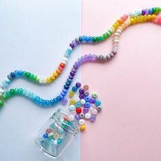 a jar filled with lots of beads next to a string of beads on a pink and white background