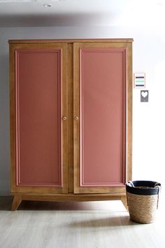 an armoire with two doors and a basket on the floor in front of it