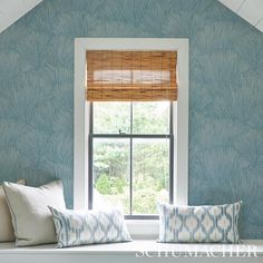 a window seat with two pillows on it in front of a blue wallpapered room