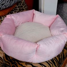 a pink dog bed sitting on top of a leopard print pillow