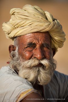 an old man with a white turban on his head is looking at the camera