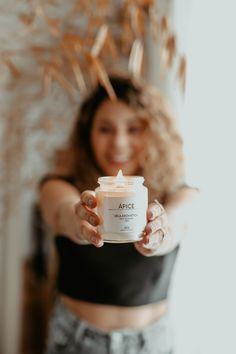 a woman holding up a candle in front of her face while wearing grey shorts and a black crop top