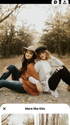 two women are sitting on the ground in front of some trees and one is wearing a hat