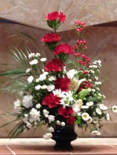 a vase filled with red and white flowers on top of a tiled floor next to a wall