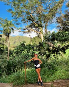 a woman posing for a photo in front of some trees and bushes with a pole