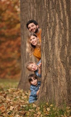 a man and two children standing next to each other near a tree with leaves on the ground