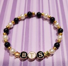 a beaded bracelet with the letter b is shown in gold and black beads on a striped background