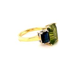 A beautiful pairing of bright colors and sleek shapes form this modern version of a classic 3-stone ring. This stylish ring features a gorgeous, 5.12 carat emerald-cut peridot flanked on either side by emerald-cut rich blue sapphires. The peridot has been set in yellow gold to highlight its warm color, while the blue sapphires have been set in striking white gold, creating a lovely, eye-catching contrast. So pretty and wearable! Handcrafted in 18k white and yellow gold by our Master Jewelers in Modern Green Jewelry With Accent Stones, Green Three Stone Emerald Cut Jewelry, Modern Green Emerald Ring With Accent Stones, Modern Green Rings With Prong Setting, Classic Green Multi-stone Sapphire Ring, Green Three Stone Peridot Jewelry, Green Three Stone Baguette Cut Ring, Green Peridot Three Stone Jewelry, Green Baguette Cut Three Stone Rings