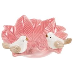 two white birds sitting on top of a pink flower shaped bowl with leaves in the background