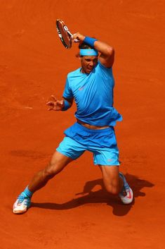 a male tennis player in blue is playing tennis on a clay court with his racket raised