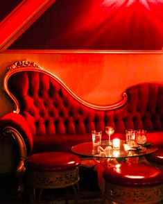 a red couch and some chairs in a room with candles on the table next to it