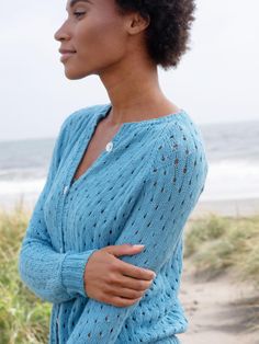 a woman standing on the beach with her arms crossed and looking off into the distance