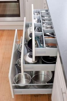 an open drawer in a kitchen filled with pots and pans on top of wooden floors