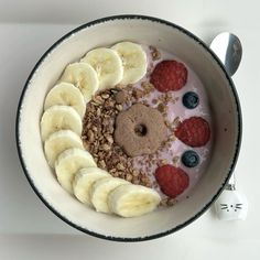 a bowl filled with yogurt and fruit on top of a white table next to a spoon