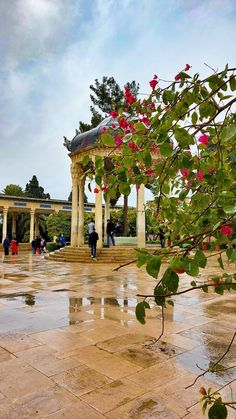 people are walking around in the rain near a gazebo with red flowers on it