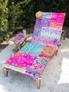 a lawn chair with a colorful blanket on it next to a small table and shrubbery