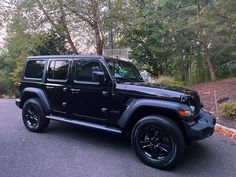 a black jeep is parked on the side of the road in front of some trees